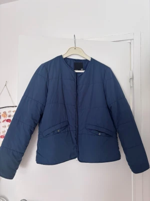 Mörkblå pufferjacka  - Snygg mörkblå pufferjacka med rund halsringning och raka ärmar. Jackan har två snedställda fickor framtill med knappstängning och quiltad design. Perfekt för kalla dagar och enkel att matcha med olika outfits.