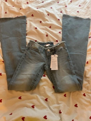 Ljusblå bootcut jeans med rå kant - Säljer ett par ljusblå bootcut jeans från Gina tricot med rå, fransad kant i midjan. Jeansen har klassisk femficksmodell, knappgylf och är tillverkade i denim med lätt tvättad look. 