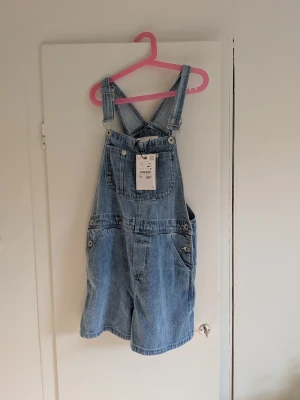 Zara hängselshorts i denim – nya med lapp 💙 - Snygga hängselshorts från Zara i ljusblå denim. Klassisk modell med justerbara axelband, ficka framtill samt flera fickor bak och på sidorna. Storlek: 12–13 år / 156 cm Skick: Nya med prislapp kvar ✨ Nypris: 299 kr Perfekta till sommaren och superfina med t-shirt eller linne under. Skriv gärna vid frågor eller om du vill ha mått!
