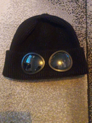 Svart ribbstickad mössa med goggles - Cool svart ribbstickad mössa med uppvikt kant och inbyggda goggles framtill. Perfekt accessoar för en streetwear-look. Tillverkad i mjukt stickat material som håller dig varm och ger en unik stil.