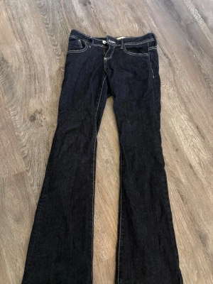 Svarta bootcut jeans med kontrastsömmar - Snygga svarta bootcut jeans med vita kontrastsömmar och klassisk femficksdesign. Jeansen har låg midja och stängs med knapp och dragkedja. Perfekta för en avslappnad och trendig look.