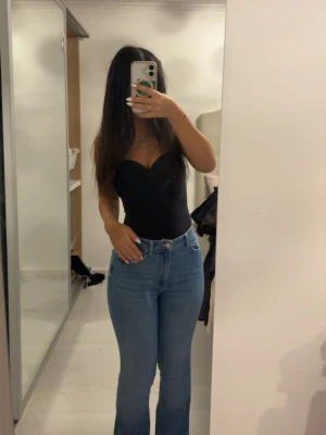 Blå bootcut jeans med hög midja - Säljer ett par klassiska blå bootcut jeans med hög midja och fem fickor. Jeansen har en snygg passform som framhäver figuren och är tillverkade i ett stretchigt denimtyg för extra komfort. Perfekta för dig som gillar en tidlös och trendig look.