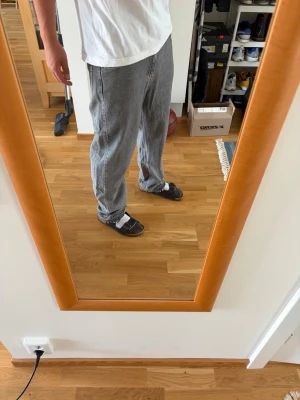 Grå baggy jeans med mönstrad ficka - Säljer ett par gråa baggy jeans med en unik svartmönstrad bakficka. Jeansen har avslappnad passform och raka ben, perfekta för en chill och trendig look. Materialet är klassisk denim och de har tydliga sömmar längs benen. Storlek: 32/32