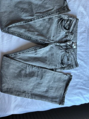 Grå flared jeans med låg midja - Säljer ett par grå jeans med flare passform och låg midja. Jeansen har klassisk femficksdesign, bälteshällor och dragkedjegylf. Materialet är denim i bomull och färgen är ljusgrå med en lätt tvättad look. Perfekta för en avslappnad och trendig stil.