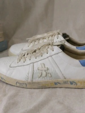 Vita sneakers med blå detalj - Snygga Premiata sneakers i storlek 44. Vita med blå detaljer och vintage-look. Nypris över 3 000 kr. Fint skick och säljs då de inte längre används. Perfekta för dig som vill ha ett par exklusiva sneakers med en unik design. Priset kan diskuteras vid snabb affär. Bara skriv om mer bilder så fixas de.