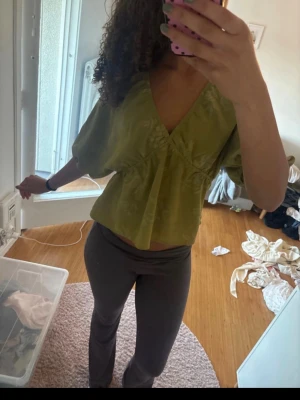 Grön omlottopp med v-ringning Zara  - Snygg grön omlottopp med v-ringning och vida, korta ärmar. Toppen är croppad och har en avslappnad passform som ger en trendig look. Perfekt att matcha med höga byxor eller kjol för en cool stil.