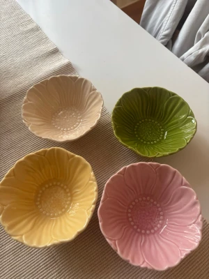 Fyra blomformade skålar i pastell - Säljer fyra små skålar i keramik formade som blommor. Skålarna är i olika pastellfärger: gul, rosa, grön och beige. Perfekta för snacks, godis eller småplock. De har fina detaljer och en blank yta.