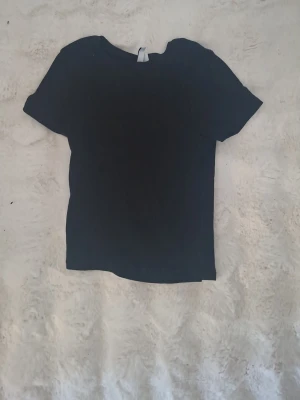 Svart basic t-shirt - En enkel svart t-shirt med korta ärmar och rund hals. Perfekt att matcha med jeans eller shorts för en clean och stilren look. Tillverkad i mjuk bomull för skön känsla hela dagen.