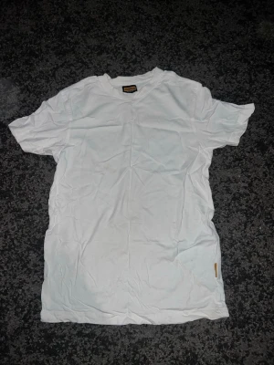 Vit basic t-shirt i bomull - En enkel vit t-shirt i mjuk bomull med rund hals och korta ärmar. Perfekt till jeans eller shorts och funkar året runt. Klassisk passform utan tryck eller mönster, bara en liten etikett i nederkant.