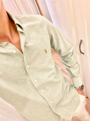 Ljusgrön skjorta från Polo Ralph Lauren (Slim Fit) - Klassisk ljusgrön skjorta från Ralph Lauren med button-down krage och broderad logga på bröstet. Skjortan har långa ärmar, normal passform och stängs med vita knappar framtill. Perfekt till jeans eller chinos för en clean look. Storlek M. Snabb Leverans!