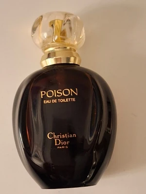 Poison Eau de Toilette från Dior Limited editon  - En lyxig parfymflaska från Christian Dior, Poison Eau de Toilette. Flaskan är mörklila med gulddetaljer och har en elegant, rundad form med en transparent, kristalliknande kork. Rymmer 50 ml och utstrålar exklusivitet och klass. Ordinarie pris: 1500kr