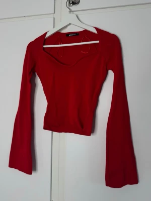 Röd långärmad topp med vid urringning - Trendig röd topp med lång ärm och vid, djup urringning. Modellen är figurnära och har en något croppad passform. Perfekt för dig som vill sticka ut med en färgstark och stilren look.