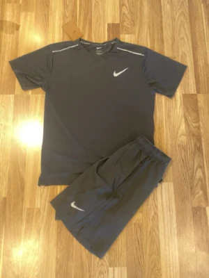 Svart set från Nike - Snyggt svart set från Nike med t-shirt och shorts. Båda delarna har den klassiska vita Nike-loggan framtill. T-shirten har rund hals och korta ärmar, shortsen har resår i midjan för skön passform. Perfekt för dig som gillar sportig stil.
