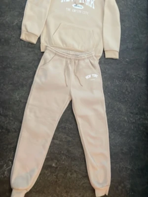 Beige loungewear set New York - Säljer ett beige loungewear set med sweatshirt och matchande byxor. Båda delarna har tryck med texten 'New York U.S.A'. Tröjan har magficka. Perfekt för chill dagar hemma eller när du vill vara bekväm. Setet har inga defekter alls och är i toppenskick