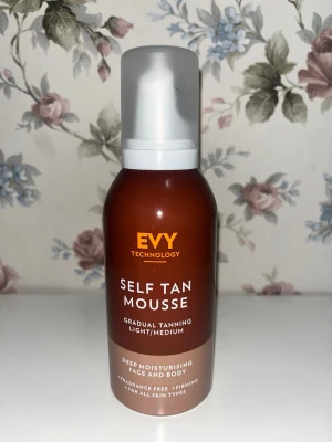 EVY Self Tan Mousse Light/Medium - EVY Self Tan Mousse är en brun utan sol-mousse för ansikte och kropp. Ger gradvis solkysst färg och återfuktar huden. Passar alla hudtyper, är parfymfri och har en lätt till medium ton. Flaskan är brun med vit pump och text i vitt och orange.
