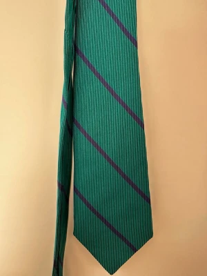 Grön slips med lila ränder - Snygg grön slips från Pierre Charron med diagonala lila linjer. Klassisk form och smal spets. Perfekt för dig som vill addera lite färg till outfiten. Materialet är 100% silke.