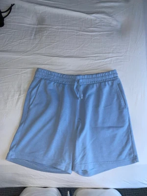 Ljusblå mjukisshorts  - Säljer ett par ljusblå mjukisshorts med elastisk midja och dragsko. Shortsen har två sidofickor fram och en bakficka. Tillverkade i mjukt sweatshirtmaterial, perfekta för chill dagar eller träning.