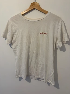Vit t-shirt med Ka-Chow tryck - Vit t-shirt med rakt snitt och rund hals. På bröstet finns ett litet tryck med texten 'KA-CHOW' och en gul blixt mellan bokstäverna. T-shirten är enkel och passar perfekt till jeans eller shorts.