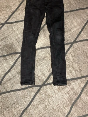Svarta skinny jeans med detaljer - Snygga svarta skinny jeans med klassisk femficksdesign och silverfärgade nitar. Jeansen har en smal passform och är tillverkade i ett stretchigt material för extra komfort. Perfekta för en trendig och stilren look. W 27 L 32