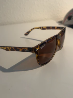RayBan boyfriend polarized leopard - Snygga Ray-Ban solglasögon med brunmelerad båge i klassisk boyfriend-stil. Glasen är bruna och bågen har ett leopardmönster som ger en cool retrovibe. Perfekt accessoar för att lyfta din stil i solen.