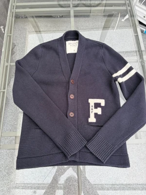 Abercrombie & Fitch Cardigan | Stl M - Säljer en superfin mörkblå varsity-cardigan från Abercrombie & Fitch! Snyggt "F"-märke på bröstet och ränder på ärmen. Storlek M. Mjuk och skön kvalitet (bomullsblandning med 5% angora/kaninhår). Jättefint skick! 