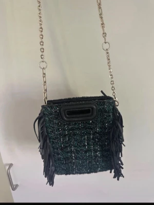 Grön tweed maje väska  - Snygg maje väska i mörkgrönt tweed tyg med svarta fransar på sidorna och guld kedjerem. Väskan har ett handtag i svart konstläder och en fyrkantig form. Väldigt unik och cool! 