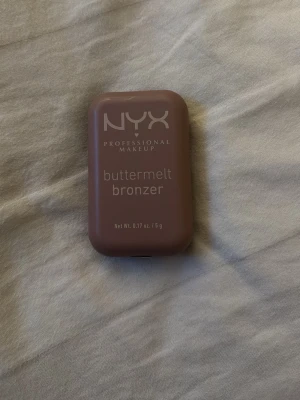 NYX buttermelt bronzer - NYX Professional Makeup buttermelt bronzer i en kompakt, rektangulär dosa med spegel. Bronzern har en varm, brun ton och en pressad yta med vågigt mönster. Köpte den utan att öppna sen när jag öppnade den insåg jag att det inte passade mig men rörde inte den ens så jag satte tillbaka klistret. Perfekt för att skapa en solkysst look och enkel att ta med i väskan.