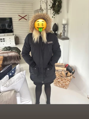 Svart Lexington dunjacka med pälskant - Säljer en äkta Lexington dunjacka i svart med huva och pälskant. Jackan har två stora fickor framtill, quiltat foder i olivgrönt och detaljer som patchar på insidan. Lång modell som går ner över höfterna och stängs med dragkedja och knappar. Finns inget kvitto från köpet men den är köpt direkt ur butik för 6999kr jag har inte så bra koll på hur man kollar Lexington jackor men vet att det är en äkta jacka så innan du vill köpa så får du gärna kolla till om den är äkta för din egen skull.