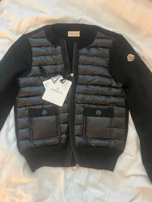 Svart cardiganjacka från Moncler - Snygg svart cardiganjacka från Moncler med quiltad framsida och två fickor med knappar. Jackan är helt ny med prislapp! Storlek s
