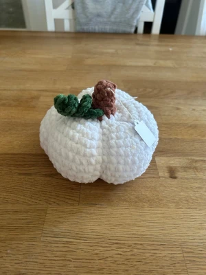 Virkad vit pumpa - Handgjord pumpa i orange, virkat av mjukt och fluffigt garn. Dekorerad med ett brunt skaft och grönt blad på toppen. Perfekt som höstdekoration eller till halloween. Söt och unik inredningsdetalj som passar på bord eller hylla.