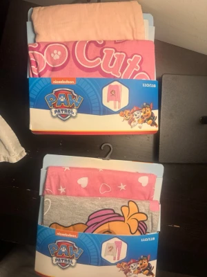 Paw Patrol pyjamas set rosa/grå 110/116 - Två söta Paw Patrol pyjamas-set för barn i storlek 110/116. Ena setet är rosa med texten 'So Cute' och motiv, det andra är grått och rosa med Skye-tryck och hjärtan. Perfekta för mysiga kvällar och pyjamasparty!
