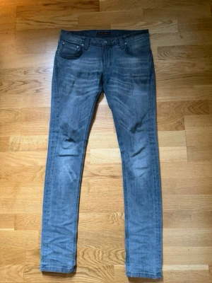 Grå nudie jeans - Säljer ett par grå slim fit nudie jeans med klassisk femficksdesign och normal midja. Jeansen har en snygg tvättad look och raka ben. Perfekta för dig som gillar en enkel men stilren stil. Materialet är denim med lite stretch för extra komfort.