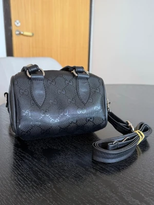 Svart Gucci mini handväska  - Säljer en gullig Gucci inspirerad väska som aldrig är använd och därmed i nyskick. Väskan har både handtag och justerbar axelrem i svart konstläder samt silverfärgade metalldetaljer. Perfekt för dig som gillar trendiga accessoarer. Pris kan diskuteras vid snabb affär! 🌸