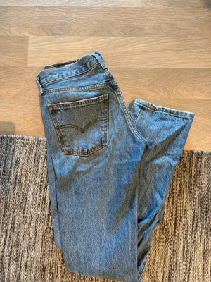 Levis jeans - Säljer ett par klassiska blå jeans från levis i modellen Middy Straight. Jeansen har raka ben, fem fickor och normalhög midja. Tillverkade i slitstark denim med snygga kontrastsömmar. Perfekta för en avslappnad och trendig look.
