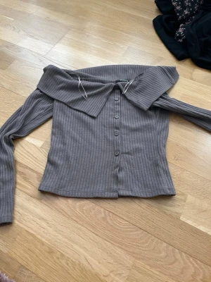 Brun ribbad off shoulder-tröja Gina Tricot - Säljer en brun ribbad tröja från Gina Tricot med off shoulder-design och stora krage. Tröjan har långa ärmar, knappar framtill och är gjord i ett mjukt, stretchigt material. Perfekt för dig som gillar trendiga detaljer och en snygg siluett.
