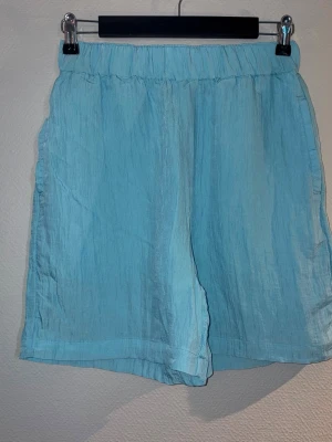 Ljusblåa krinklade shorts  - Säljer ett par ljusblå krinklade shorts med loose passform och resår i midjan och 2 fickor, perfekta för varma dagar. Shortsen har en enkel och avslappnad look som passar till det mesta.