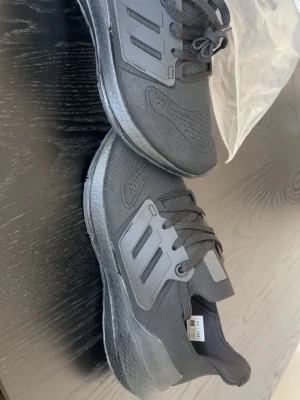 Svarta Adidas Ultraboost sneakers - Snygga svarta Adidas Ultraboost sneakers med stickad ovandel och klassiska tre ränder på sidan. Skorna har en bekväm Boost-sula och snörning framtill. Perfekta för dig som gillar sportig och stilren look.
