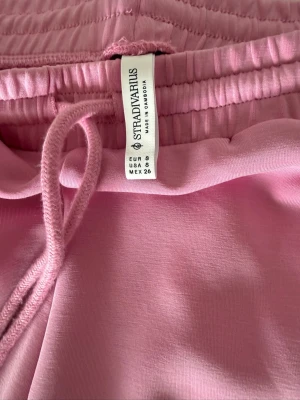 Rosa mjukisbyxor från Stradivarius - Säljer ett par ljusrosa mjukisbyxor från Stradivarius med dragsko i midjan och sidofickor. Byxorna har en relaxed fit och är gjorda i mjukt, stretchigt material som är perfekt för chill dagar. Klassisk design med ribbad midja och raka ben. Denna färg är slut överallt. Aldrig använda och köpta i Spanien i butik. 