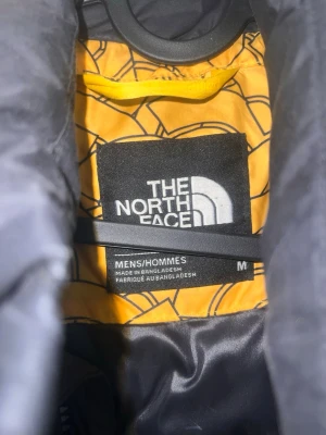 Gul och svart pufferjacka The North Face - Säljer en gul och svart pufferjacka från The North Face i storlek M. Jackan har ett unikt grafiskt mönster, hög krage och dragkedja framtill. Två sidofickor med dragkedja och klassisk logga på ärmen. Perfekt för kalla vinterdagar. Har lite små defekter 