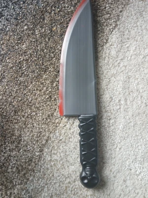 Plastkniv för maskerad med bloddetalj - Cool plastkniv som accessoar till maskerad eller cosplay. Kniven är grå med röd blodliknande detalj längs bladet och har ett svart handtag med dödskallemönster. Perfekt för halloween eller skräcktema.