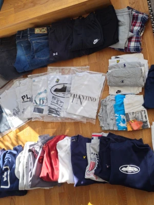 Stort klädpaket med märkeskläder och annat för Ungdomar - Säljer ett stort klädpaket med jeans, shorts, t-shirts, hoodies och pikétröjor från märken som Nike, Under Armour, Champion, Ralph Lauren, Valentino och Fortnite. Färgerna varierar mellan blått, grått, vitt, rött och svart. Perfekt för dig som vill uppdatera garderoben med snygga och trendiga plagg. Otroligt många fina välskötta varor som söker nya ägare! Skriv till mig om ni vill ha storlekar osv. Jag svarar snabbt och säljer till ett rimligt pris.