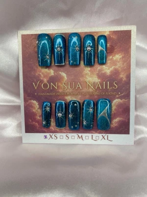 Nyra (XS);Medium Square - Unika handgjorda press-on naglar i glittrande cateye blå färg och handmålade silvriga små stjärndetaljer. Naglarna har en medium lång square form och dekoreras med små silverpärlor och konstnärliga mönster. Perfekt för dig som vill ha en kreativ och trendig look.XS: 14 mm, 11 mm, 11,5 mm, 10 mm, 8 mm, tummlängden 23mm.
