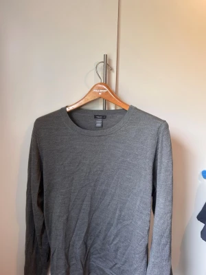 Grå stickad tröja från Filippa K - Snygg grå stickad tröja från Filippa K i 100% merinoull. Tröjan har rund halsringning och långa ärmar, perfekt för lager på lager och enkel att matcha med olika outfits. Stilren och tidlös design som passar till det mesta.