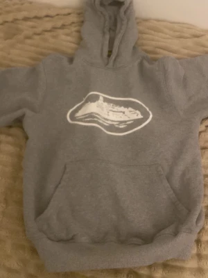 Grå hoodie med vit grafisk print - Säljer en grå hoodie med huva och stor magficka. På bröstet finns ett vitt grafiskt tryck i form av en våg eller landskap. Hoodien har ribbade muddar vid ärmar och nederkant. Perfekt för en avslappnad och chill stil.