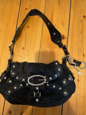 Svart handväska Guess - Så snygg handväska från Guess! Perfekt size. Tappat nån liten bit läder på insida axel + rostat på på små ställen på insidan (syns inte). Ringen som är lite rostad kan knipsas av, vet inte vad det är för nått! 