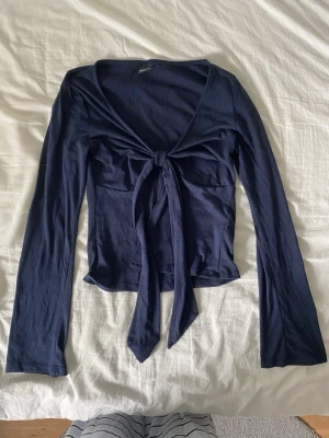 Mörkblå långärmad topp med knyt - Snygg mörkblå långärmad topp med v-ringning och knyt framtill. Perfekt att styla med jeans eller kjol för en trendig look.