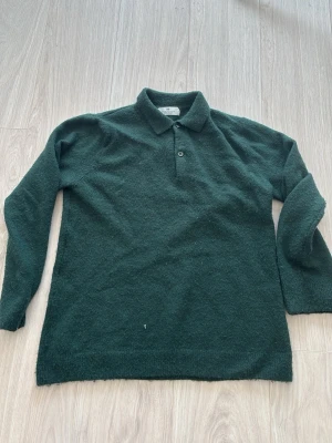 Mörkgrön stickad tröja med krage - Mysig mörkgrön stickad tröja med klassisk krage och knappslå framtill. Långärmad modell i mjukt material som passar perfekt till både jeans och kjol. Enkel och stilren design utan mönster eller extra detaljer.