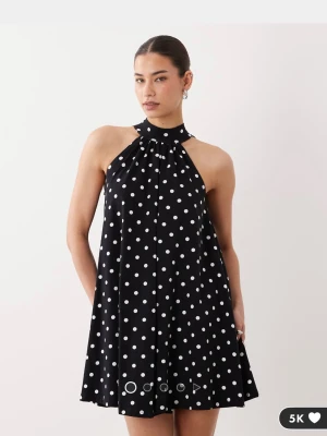 Svart prickig halterneckklänning - Snygg svart kortklänning med vita prickar och halterneck. Klänningen har en lös passform och är ärmlös, vilket ger en luftig och trendig look. 