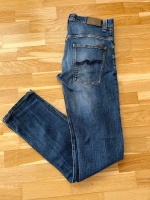 Nudie Jeans - W34 L36 - Snygga mörkblå jeans från Nudie Jeans. Klassisk och stilren modell med snygga kontrastsömmar och ikonisk Nudie-detalj på bakfickan.  📏 Storlek: W34 L36 🎨 Färg: Mörkblå 👖 Passform: Slim ✨ Skick: Mycket fint skick, inga tydliga skador eller hål