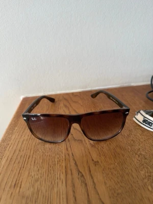 Bruna solglasögon från Ray-Ban - Snygga solglasögon från Ray-Ban med brunt, transparent plastbåge och rektangulära glas. Glasen har en snygg toning från mörkbrunt till ljusare nedtill. Perfekta för soliga dagar och ger en cool vibe till din outfit.